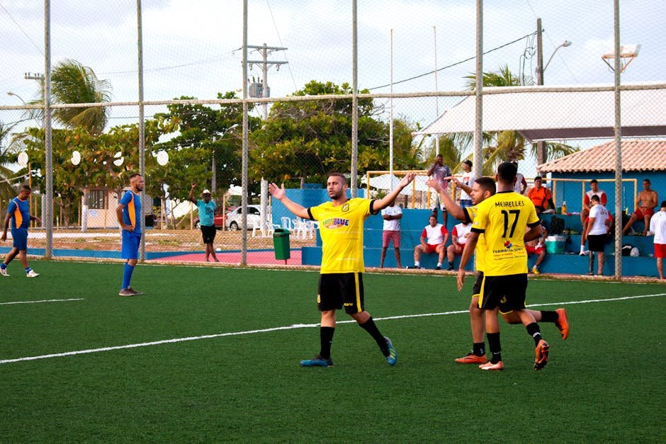Amateur soccer team in yellow jerseys celebrates a goal during a match on an outdoor field.