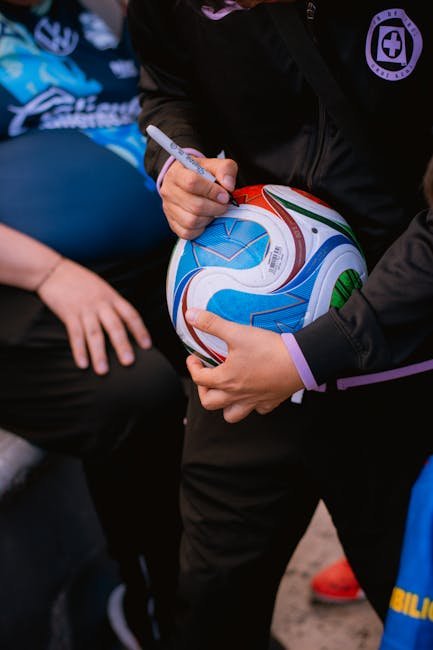 Close-up of a soccer player signing an autograph on a colorful soccer ball.