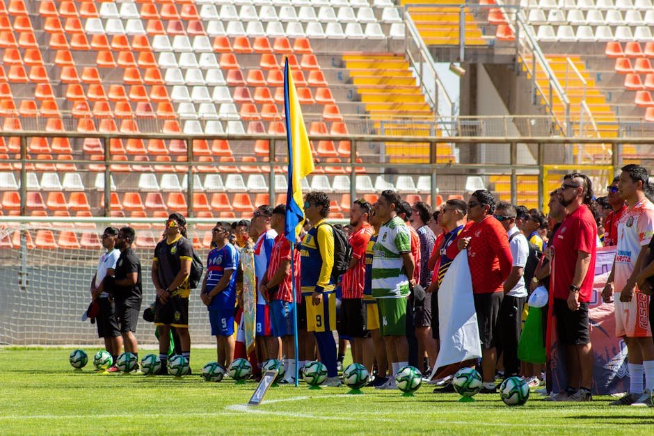 Multiple soccer teams stand in line in a brightly lit outdoor stadium for a ceremony or event.