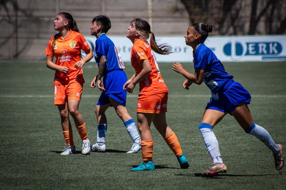 Female soccer players in vibrant uniforms compete on an outdoor field during daylight.