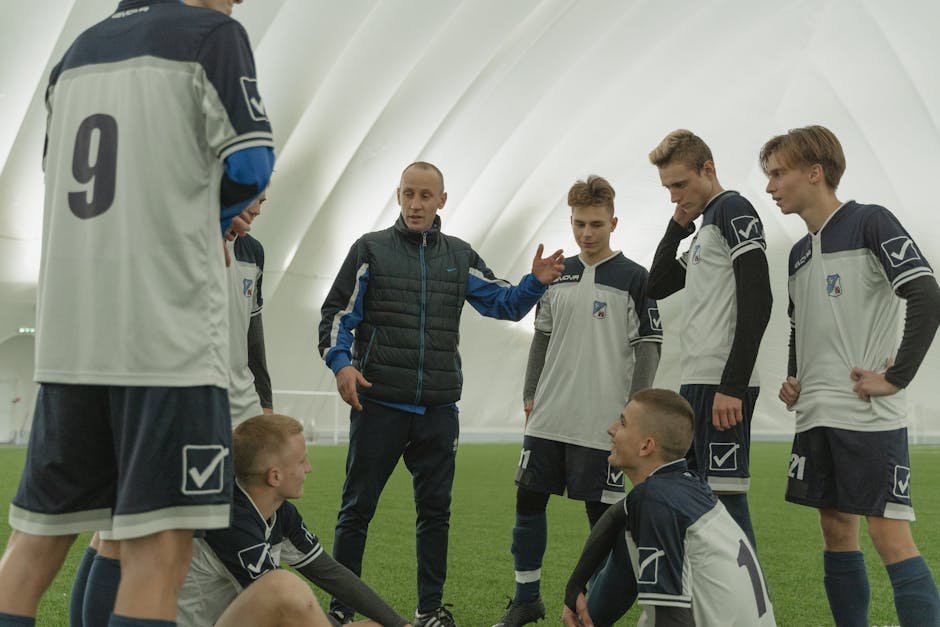 A coach passionately instructs his soccer team during a practice session inside a sports dome.